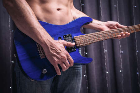 Six-pack man posing with a blue electric guitar. Rock concerts concept. Mixed mediaの写真素材