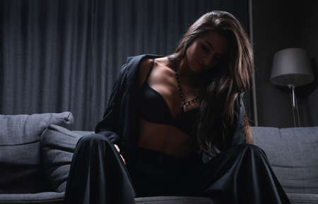 Image of a stylish beautiful brunette sitting on a sofa. Business suit and sexy underwear. Mixed mediaの写真素材