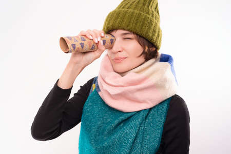 Portrait of smiling woman in winter hat and scarf looking through festive wrapping paper. Holidays concept. Mixed mediaの写真素材