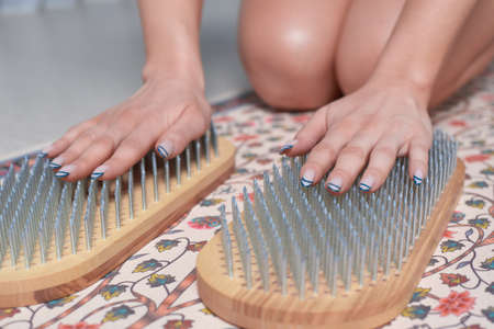 Image of a young woman in a gymnastic suit sitting on a mat in a bright studio preparing for meditation with a sadhu board. The concept of fitness, yoga, pilates. mixed mediaの写真素材