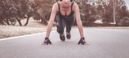 Image of a girl in headphones who stands in a lower position before starting to run. The concept of...