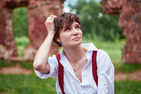 Image of a stylish beautiful woman in a white shirt, black trousers and red suspenders sitting in a...
