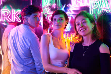 Image of two beautiful women and one man in an amusement park in a room with neon light. entertainment concept. mixed mediaの写真素材