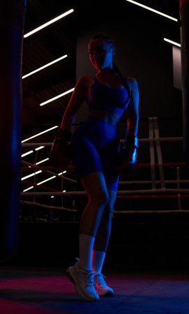 Powerful girl poses near the bag on the background of the ring. color flashes. The concept of wrestling and boxing. mixed mediaの写真素材