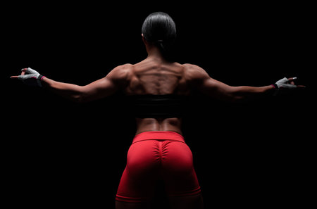 Athletic young woman showing back and arm muscles on isolated black background. mixed mediaの写真素材