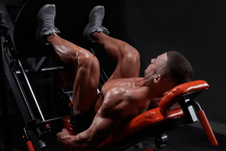 Side view of muscular ethnic male athlete lying on leg press machine and pumping muscles during workout in gym. mixed mediaの写真素材