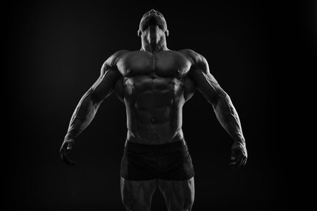 Silhouette of a strong bodybuilder. Confident young fitness athlete with a powerful body and perfect abs. Black and white photography. Dramatic light. Mixed mediaの写真素材