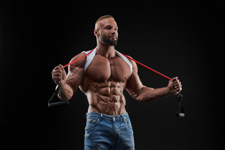 Muscular guy stretching rubber resistance bands in dark background. Perfect body. Mixed mediaの写真素材