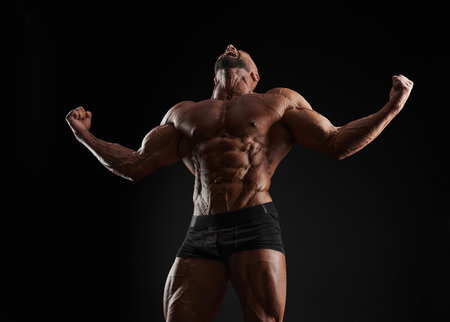 Handsome strong athletic men pumping up muscles. Workout, bodybuilding concept. Black background. Mixed mediaの写真素材