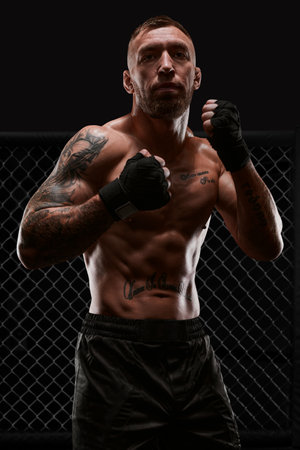 Conceptual image of a kickboxer. A real fighter stands in the real cage of the octagon. The concept of mixed martial arts, kickboxing, sports schools. Mixed mediaの写真素材
