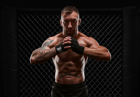 Conceptual image of a kickboxer. A real fighter stands in the real cage of the octagon. The concept of mixed martial arts, kickboxing, sports schools. Mixed mediaの写真素材