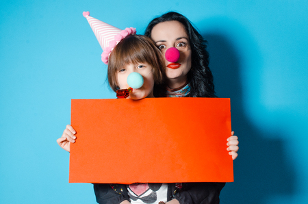 Mom and daughter celebrate their birthday. Festive outfits. The concept of a holiday. Daughter and mother mimic in the hands of an empty leafの写真素材