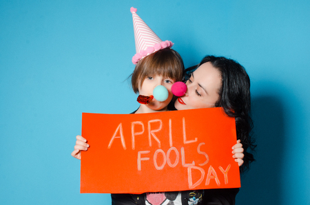 Happy mother with her daughter holding a red sheet of paper with the inscription April Fool's Day. Spring day is a fool. The concept of a holidayの写真素材