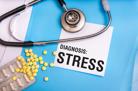 Stress word written on medical blue folder with patient files, pills and stethoscope on backgroundの写真素材