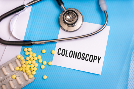 Colonoscopy word written on medical blue folder with patient files, pills and stethoscope on backgroundの写真素材