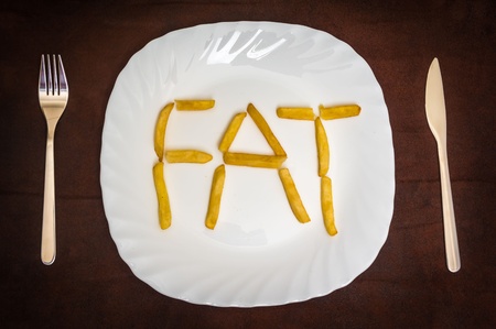 Fork, knife and french fries forming word FAT on white plateの写真素材