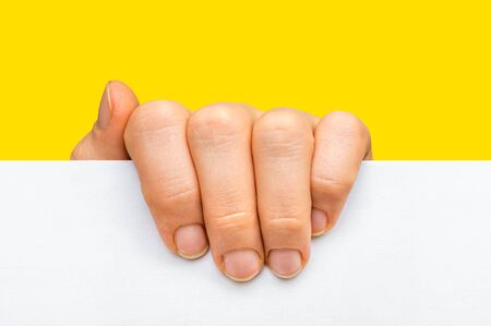 Woman's hand holding white blank paper isolated on yellow backgroundの写真素材