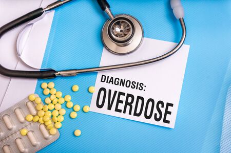 Overdose word written on medical blue folder with patient files, pills and stethoscope on backgroundの写真素材