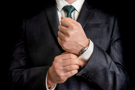 Business man fixing his cufflinks - isolated on black backgroundの写真素材