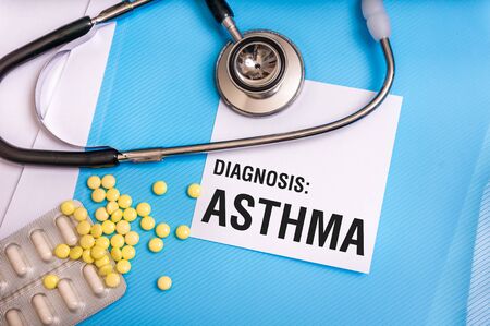 Asthma word written on medical blue folder with patient files, pills and stethoscope on backgroundの写真素材