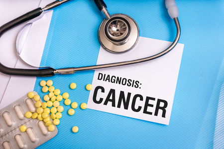Cancer word written on medical blue folder with patient files, pills and stethoscope on backgroundの写真素材