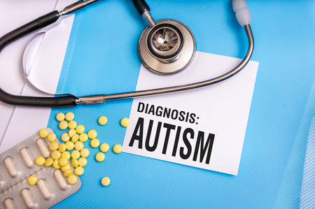 Autism word written on medical blue folder with patient files, pills and stethoscope on backgroundの写真素材
