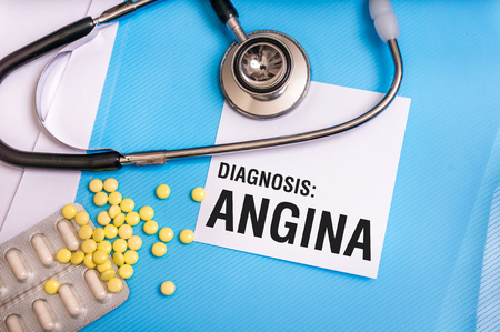 Angina word written on medical blue folder with patient files, pills and stethoscope on backgroundの写真素材