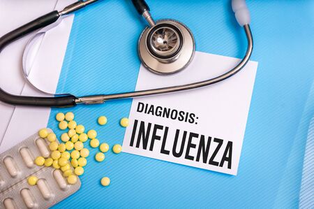 Influenza word written on medical blue folder with patient files, pills and stethoscope on backgroundの写真素材