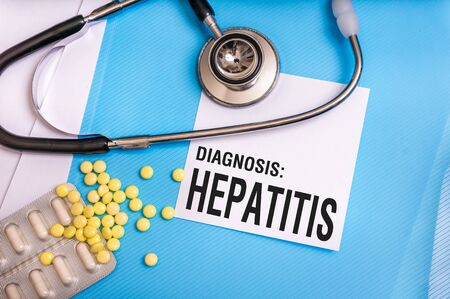 Hepatitis word written on medical blue folder with patient files, pills and stethoscope on backgroundの写真素材