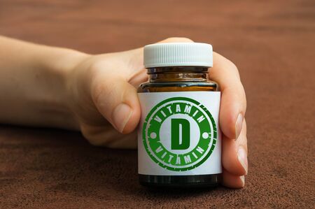 Human hand holding a bottle of pills with vitamin D on brown backgroundの写真素材