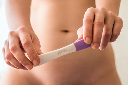 Pregnant woman holding positive pregnancy test in the bedroomの写真素材