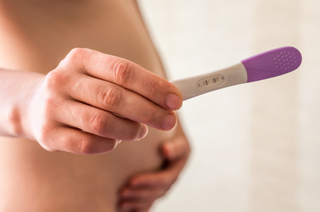 Pregnant woman holding a pregnancy test in the bedroomの写真素材