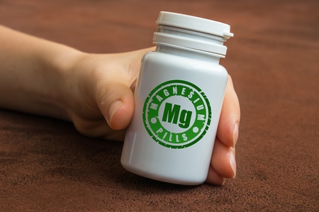 Human hand holding a bottle of pills with magnesium on brown backgroundの写真素材