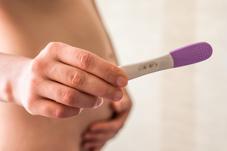 Pregnant woman holding a pregnancy test in the bedroomの写真素材