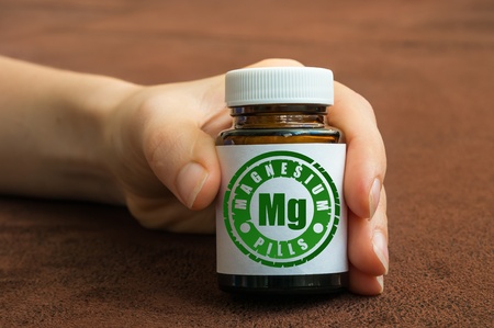 Human hand holding a bottle of pills with magnesium on brown backgroundの写真素材