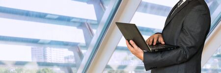 Businessman in black suit holding laptop in officeの写真素材