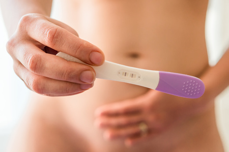Pregnant woman holding positive pregnancy test in the bedroomの写真素材