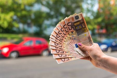 Car buyer holding euro banknotes and buying a new car from salesman on blurred backgroundの写真素材