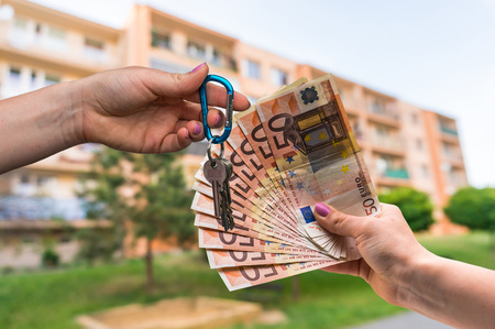 Real estate agent giving apartment keys to a new property owner, who is paying by euro money on blurred backgroundの写真素材