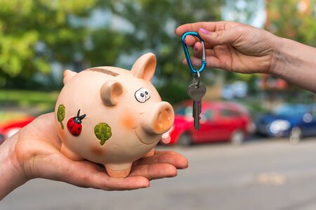 Salesman giving car keys to a new car owner, who is paying all saving money from piggy bank on blurred backgroundの写真素材