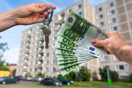 Real estate agent giving apartment keys to a new property owner, who is paying by euro money on blurred backgroundの写真素材
