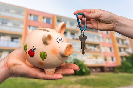 Real estate agent giving home keys to a new property owner, who is paying all saving money from piggy bank on blurred backgroundの写真素材