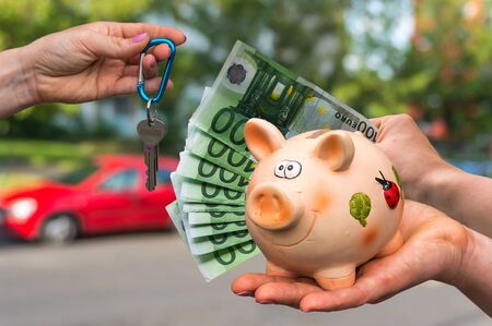 Salesman giving car key to a new car owner, who is paying last saving money from piggy bank on blurred backgroundの写真素材