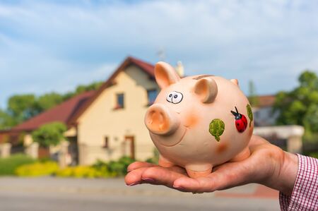 All savings money from pink ceramic piggy bank to pay for the dream house on blurred backgroundの写真素材
