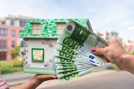 Real estate agent holding model house from paper and new property owner buying it by euro money on blurred backgroundの写真素材