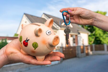 Real estate agent giving house keys to a new property owner, who is paying all saving money from piggy bank on blurred backgroundの写真素材