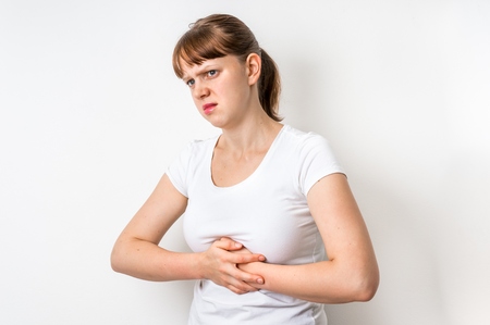 Woman with stomach pain is holding her aching bellyの写真素材