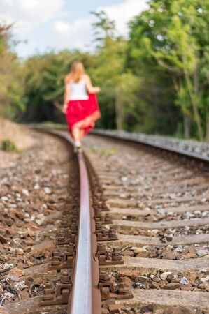 Young lady in red dress walking on railway tracksの写真素材