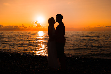 Two young lovers standing on a beach and looking to each other on sunsetの写真素材