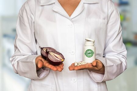 Young doctor holding fresh onion and bottle of pills with vitamins and compare themの写真素材